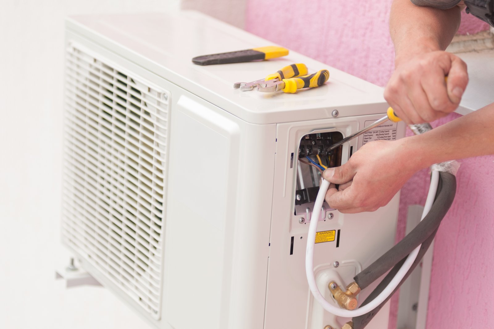 ac repair technician troubleshooting and fixing an outdoor air conditioning unit, using tools to adjust wiring and connections.